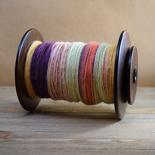 Spinning wheel bobbin filled with handspun yarn made of sheep's